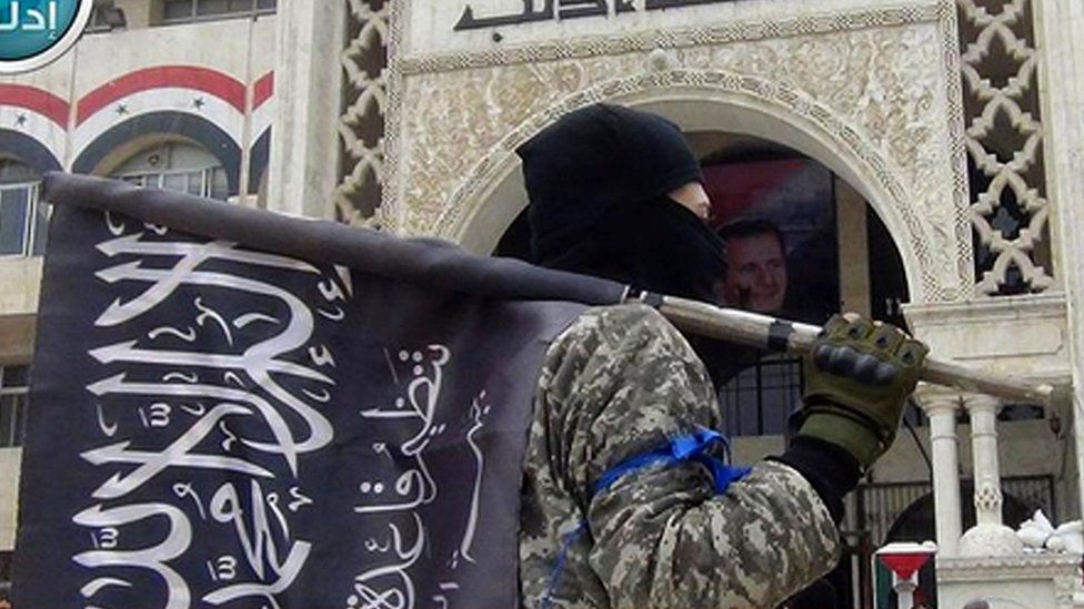 A fighter from Syria's al-Qaeda-linked Nusra Front holds his group flag as he stands in front of the governor's building in Idlib province, northern Syria