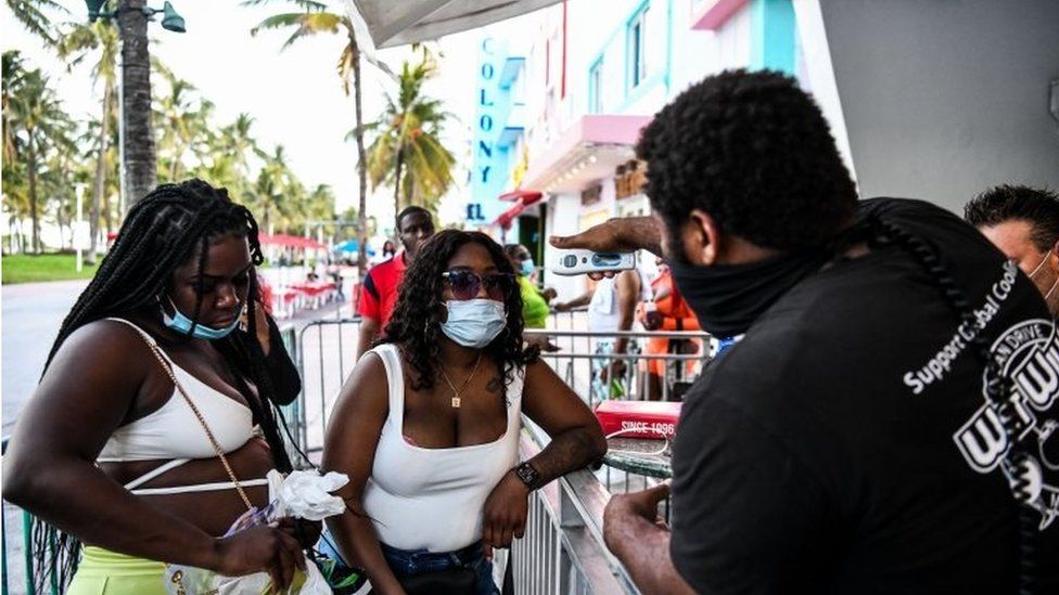 A security guard checks the temperature of a woman at the entrance of a restaurant on Ocean Drive in Miami Beach, Florida on June 24, 2020