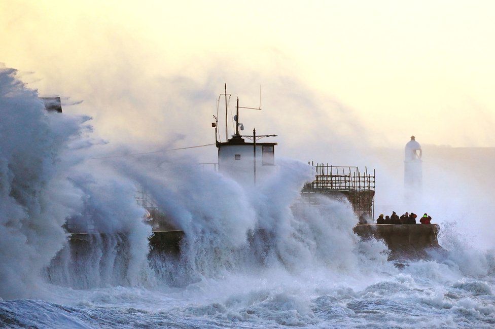 Waves crash against the sea wall and Porthcawl Lighthouse in Bridgend, south Wales