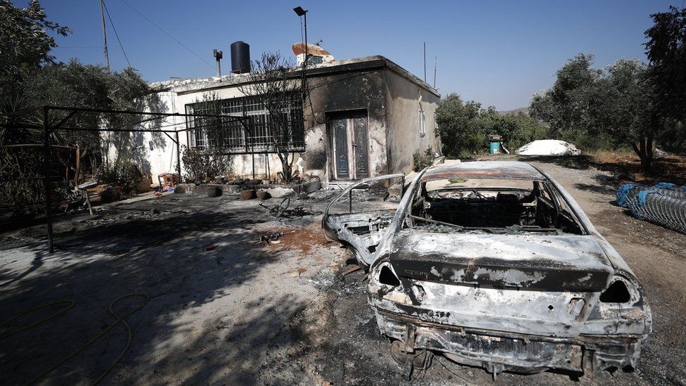 Сгоревшая машина и поврежденный дом в палестинском городе Турмус Айя на оккупированном Западном берегу после нападения израильских поселенцев (21 июня 2023 г.)