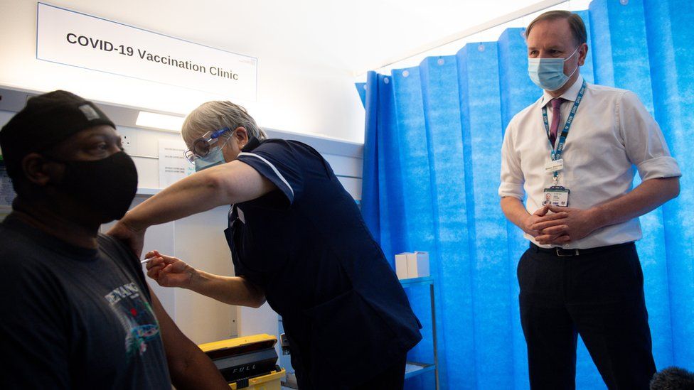 Sir Simon Stevens watches on as a man is given a vaccine