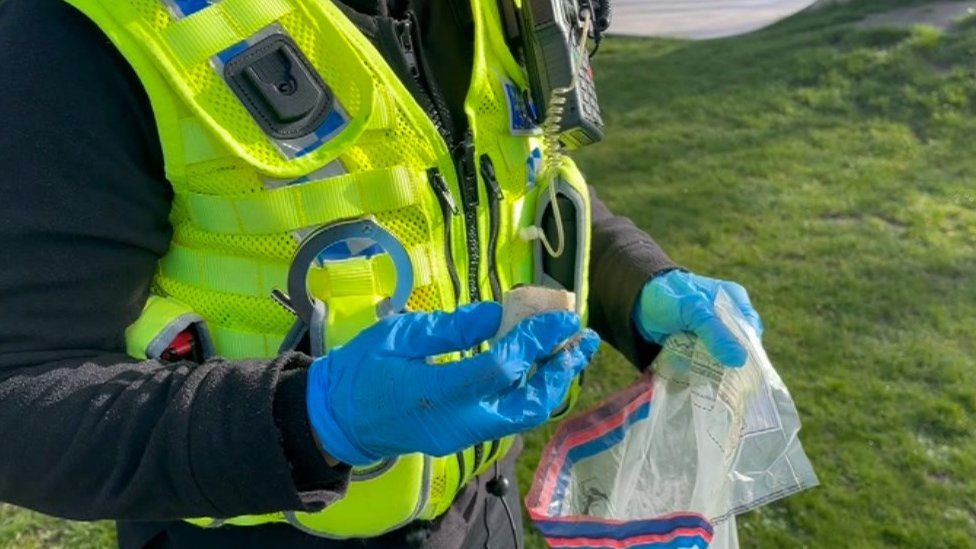 A police officer wearing a high-vis vest and holding suspected drugs