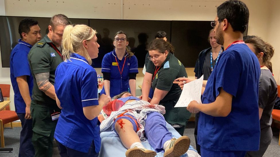 hospital workers crowded round pretend knife victim patient