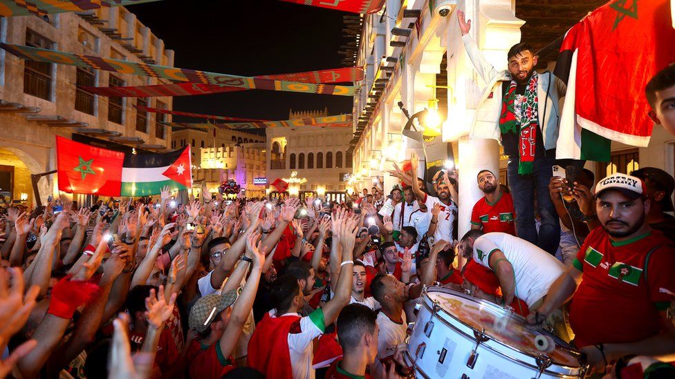 Fans raise the flag of Morocco and some are playing a big drum. There's also a Jordanian flag raised in the middle of the crowd