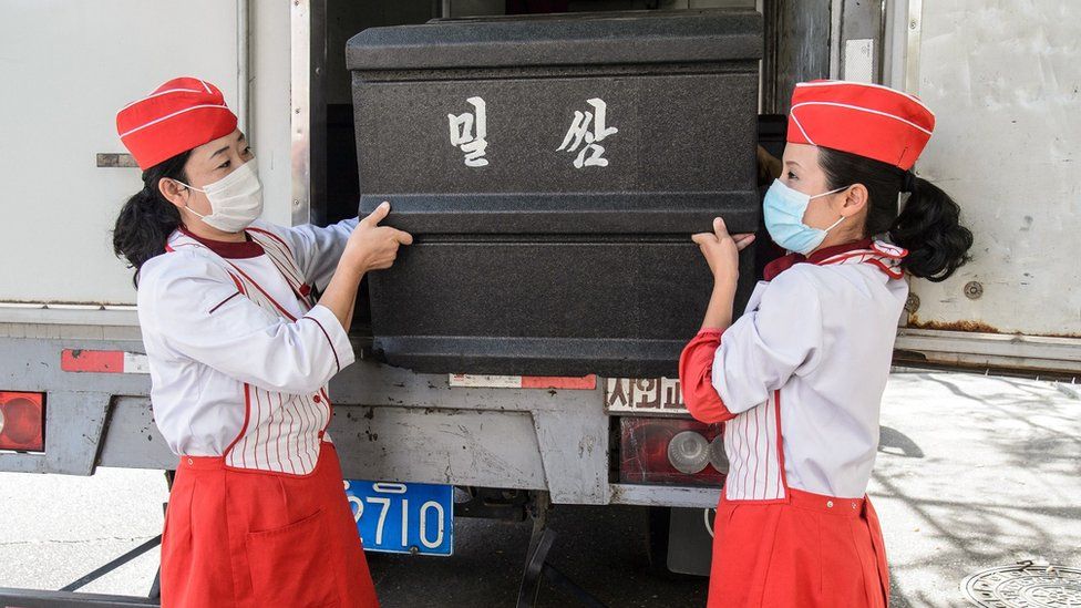 Employees carry a box of wheat cakes stuffed with meat, produced by the Kumsong Foodstuff Factory, to a movable vendor stall in the Central district in Pyongyang