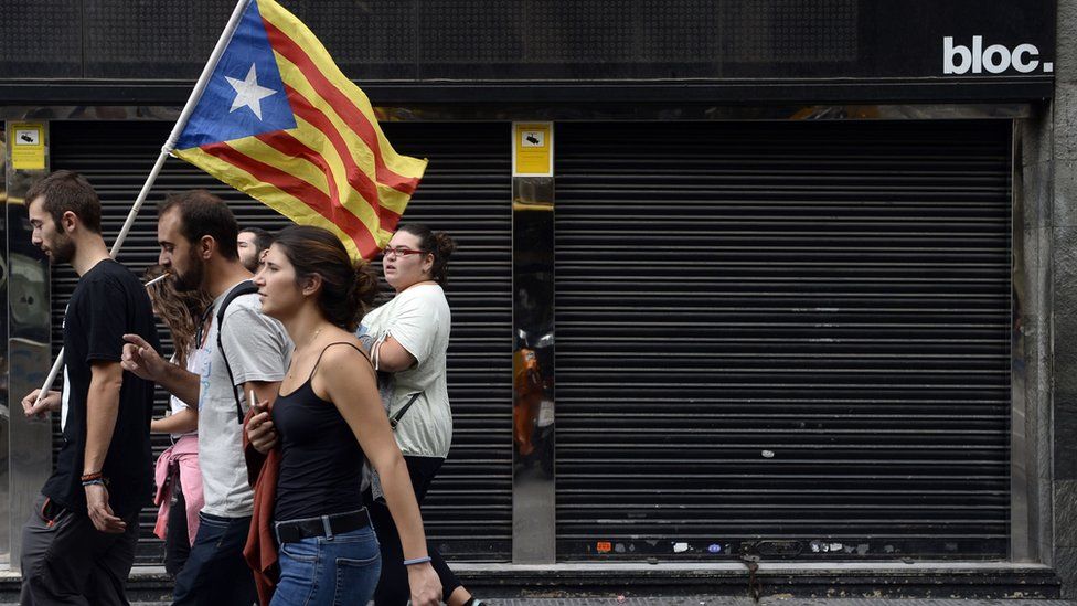 This file photo taken on 3 October 2017 shows people walking past a closed store during a general strike in Catalonia called by Catalan unions in Barcelona