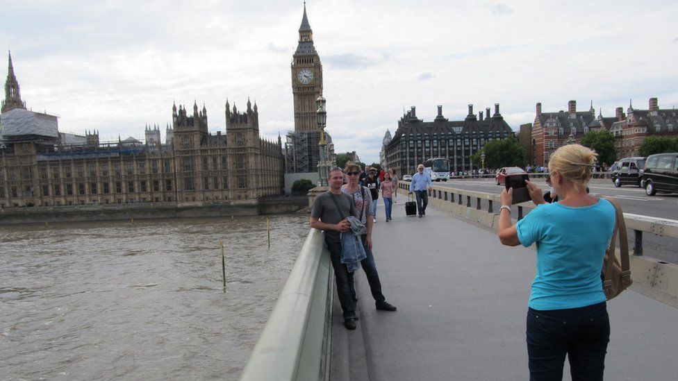 A woman taking a couple's photograph on Westminster Bridge