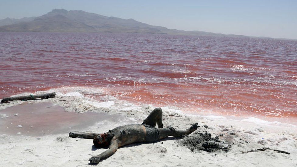 Sunbather smeared in mud on shores of a red Lake Urmia