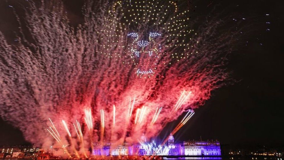 Drones and fireworks illuminate the night sky over the Old Royal Naval College