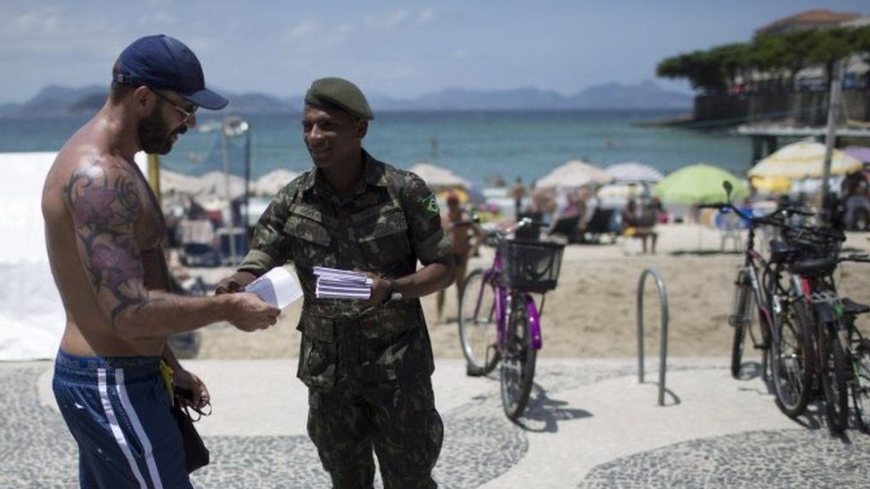 This is a Saturday, Feb. 13, 2016 file photo of an army soldier distributing a pamphlet about the Aedes aegypti mosquito that spreads the Zika virus, on the edge of the Copacabana beach, in Rio de Janeiro, Brazil.