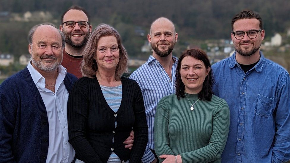 Bryan and Helena Panks smiling for a photo surrounded by their four children - three men towards the back of the images and one woman