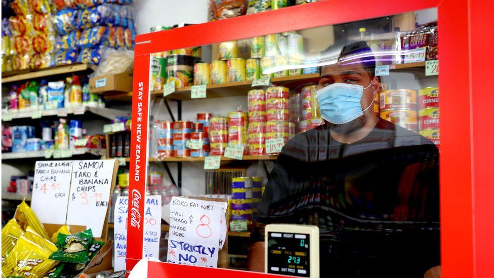 New Zealand shopkeeper with Covid-19 shield and facemask.