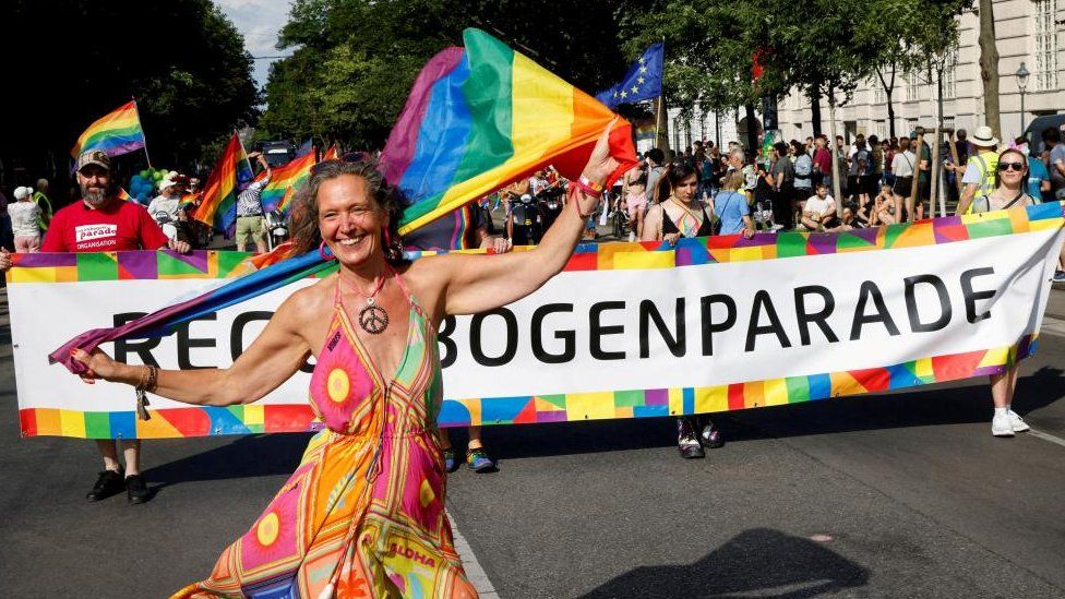 Женщина стоит с радужным флагом впереди парада гордости в Вене в субботу, 17 июня 2023 года.