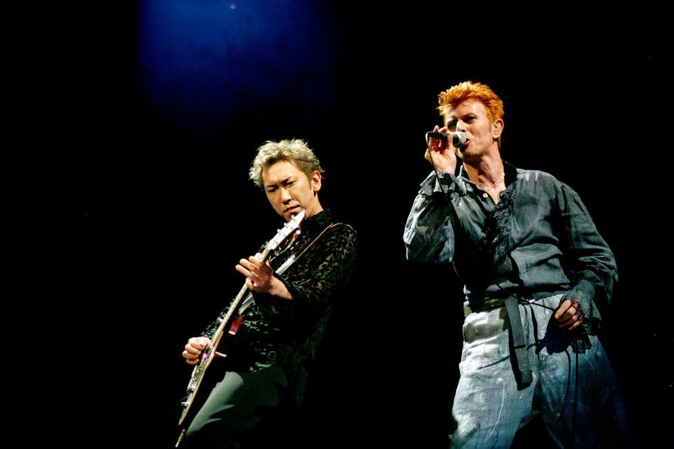 Photo of Hotei Tomayasu playing with David Bowie onstage at the Nippon Budokan in Tokyo in 1996
