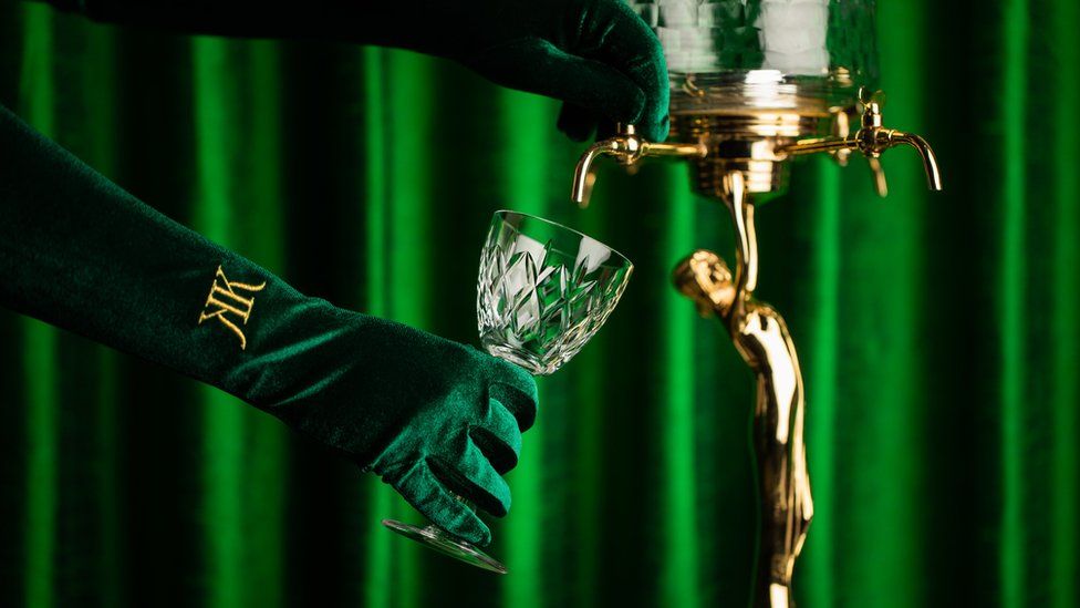 A hand in a green velvet glove dispenses a drink