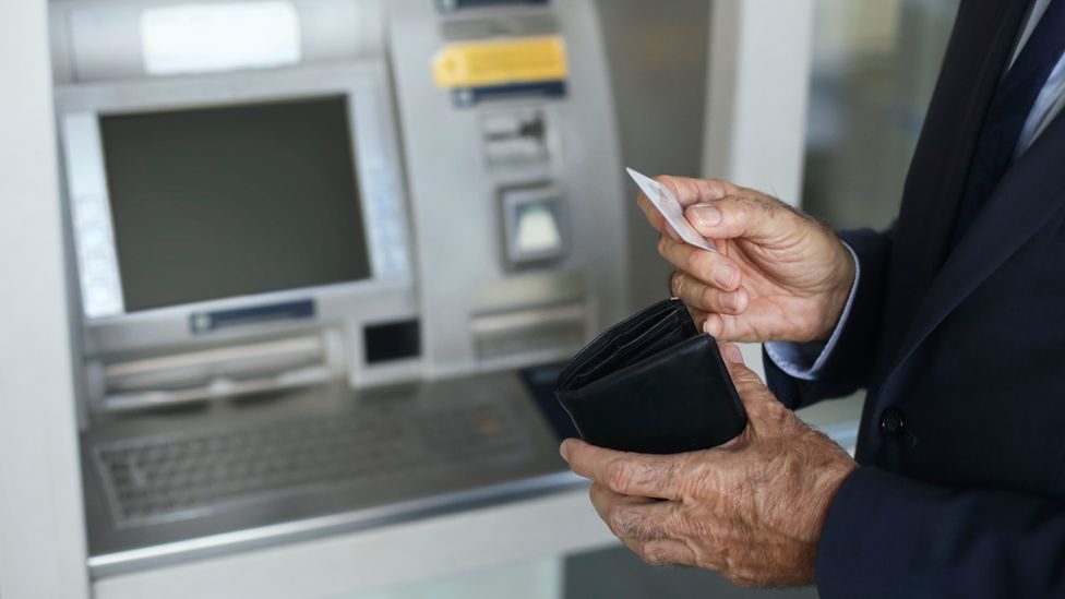 Пожилой мужчина пользуется банкоматом