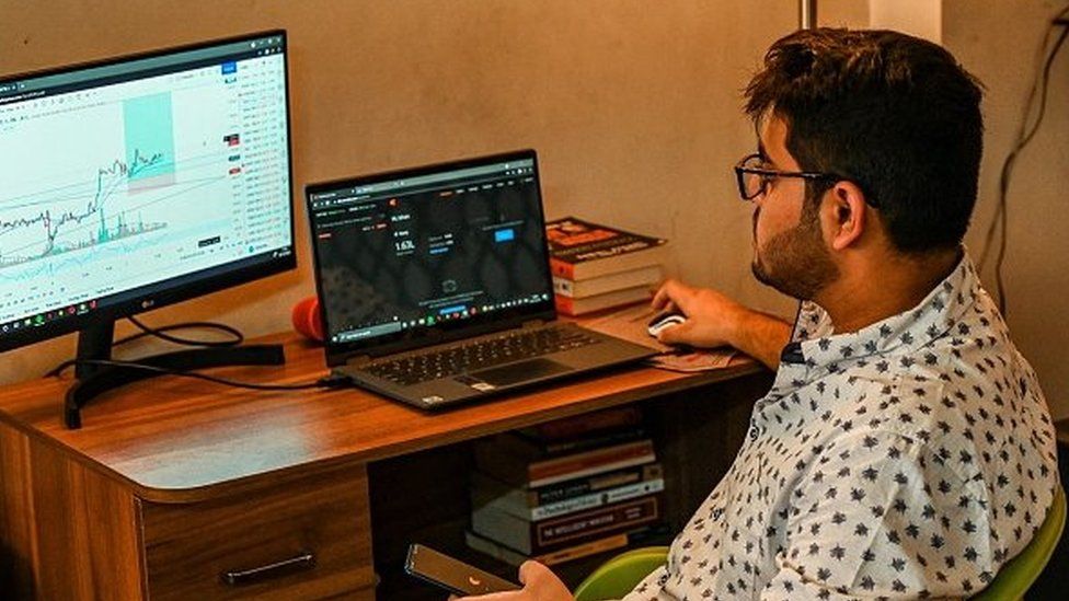 This photo taken in 2021 shows 20-year-old college student Ishan Srivastava checking stocks online on his computer, while actively trading on apps on his smart phone, at his residence in Ghaziabad.