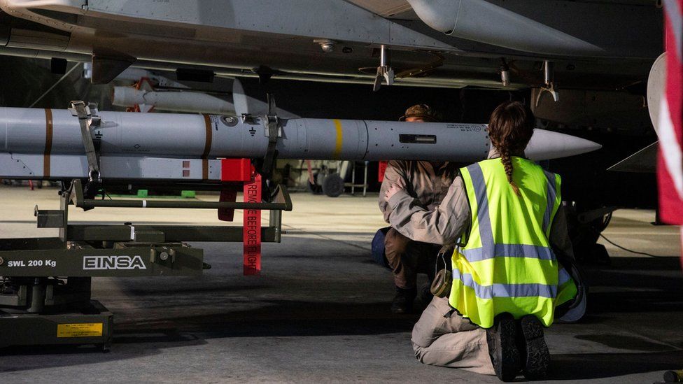 Woman kneels in front of missile attached to aircraft