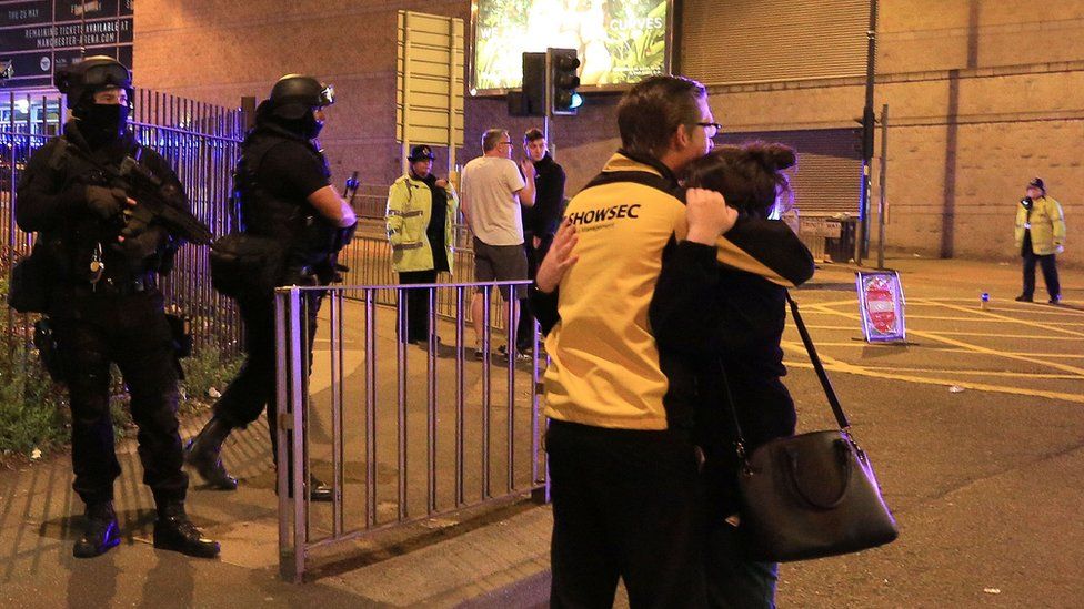 two people hug after the attack while armed officers are present