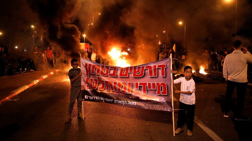 Protesters in Sderot, Israel, set fire to tyres and hold up banners to protest against the Israeli government's decision to agree to a ceasefire with Palestinian militants in Gaza (13 November 2018)