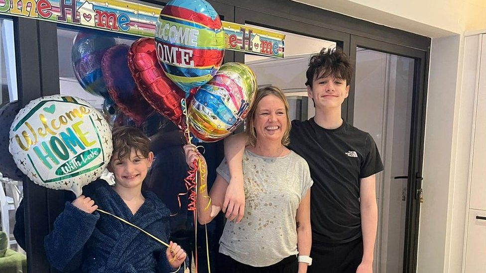 Nicola Sharpe and her sons at home surrounded by welcome home banners and balloons