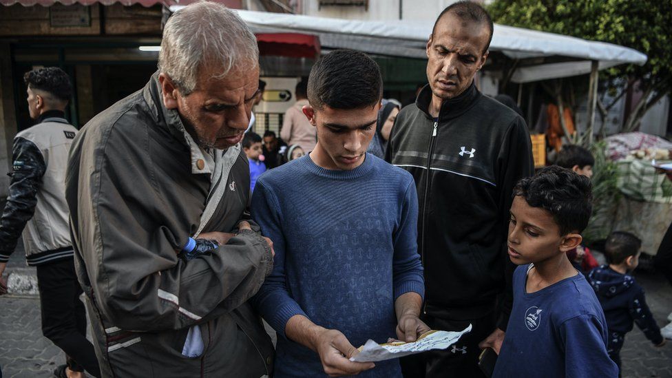 Two men and two boys on a street in Gaza look at a leaflet containing an IDF evacuation warning