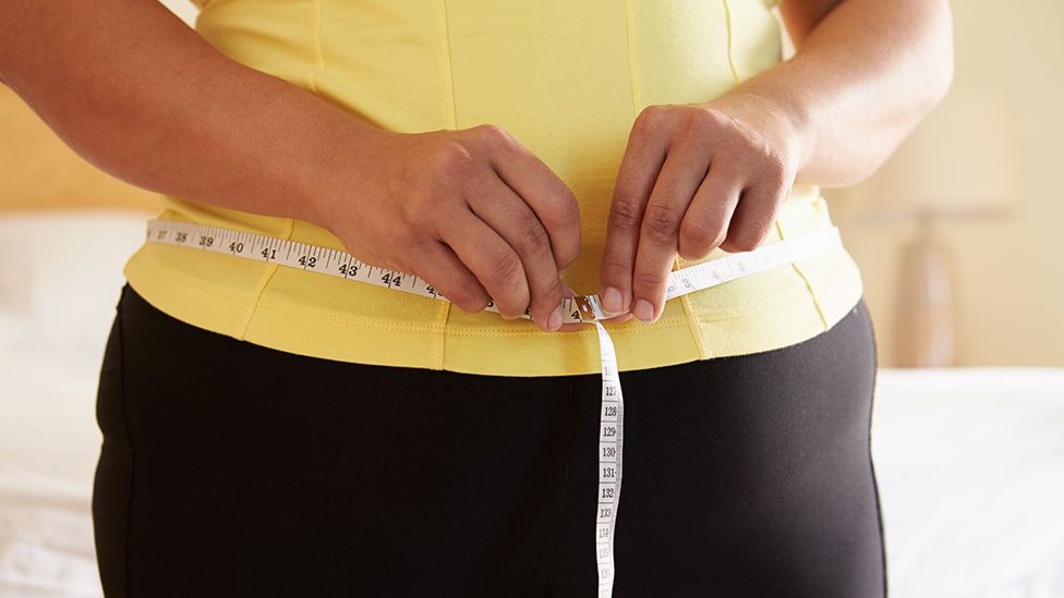 Woman (face unseen) holding tape measure across her waist