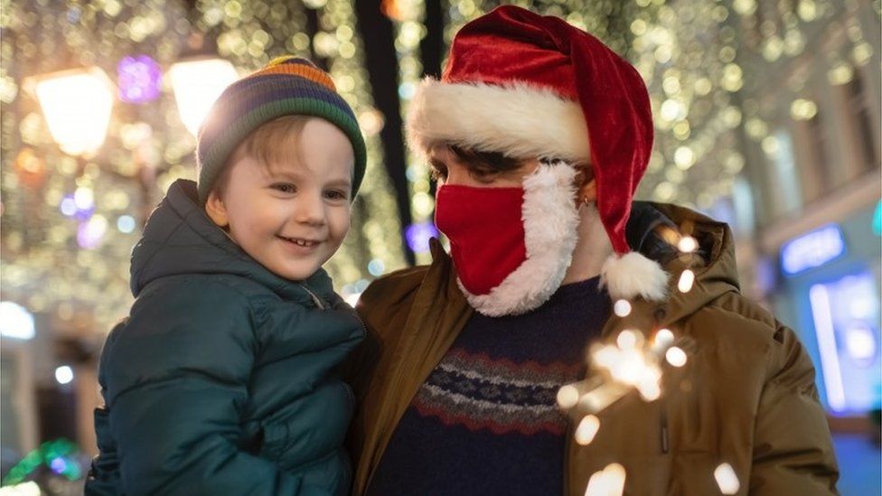 Father in Santa hat and mask holding son