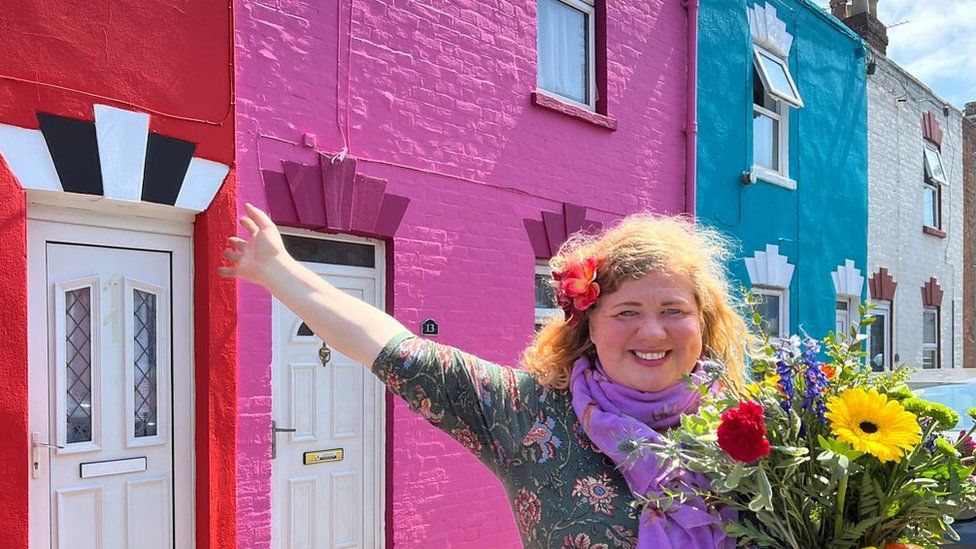 Rainbow coloured houses with women smiling stood in front of them