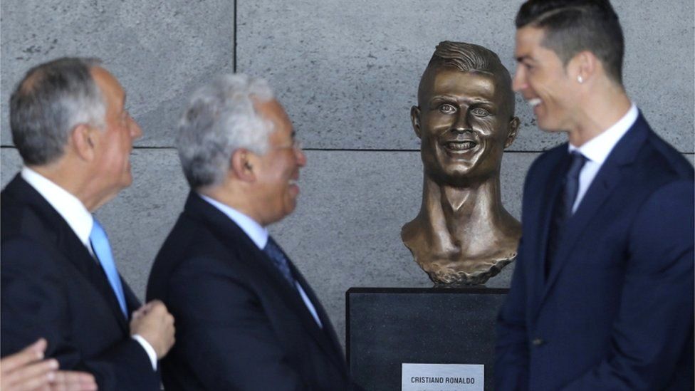 Ronaldo stands out of focus in front of his bust at the airport