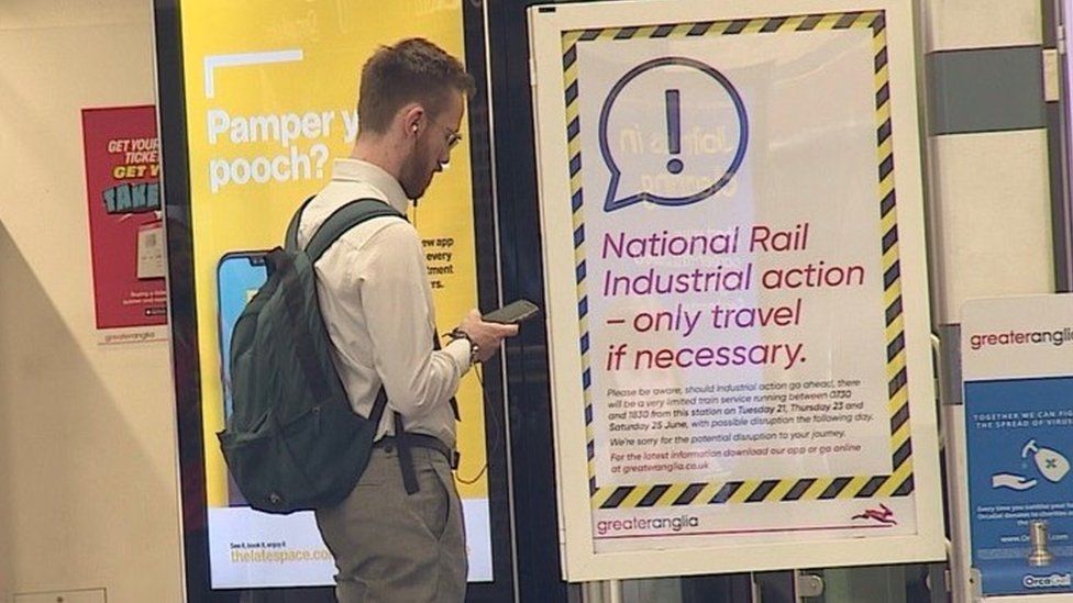 man checks phone in front of information sign about rail strike