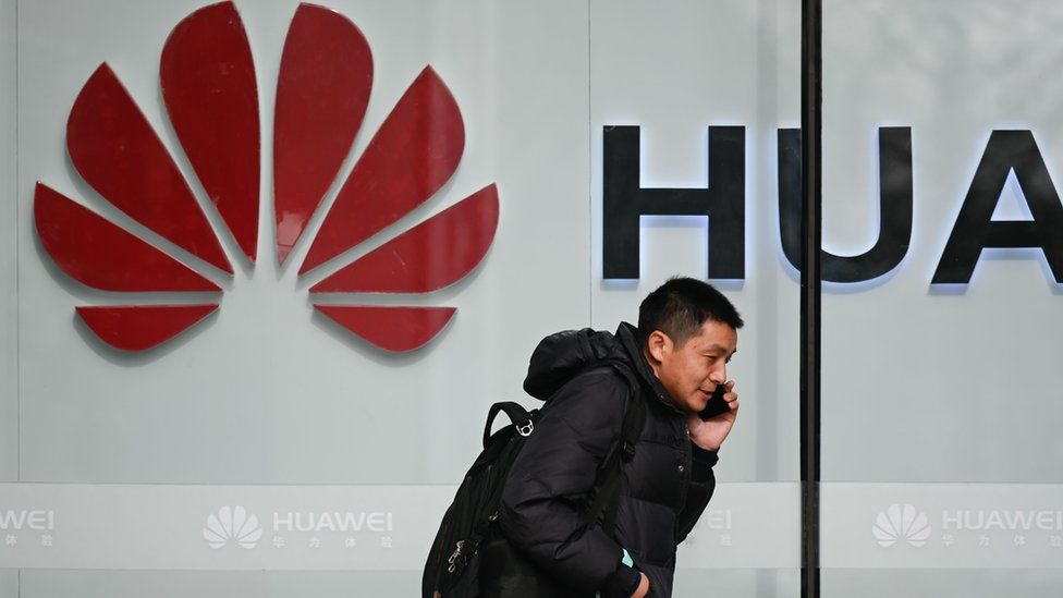A pedestrian talks on his phone while he walking past a Huawei store in Beijing on January 30, 2019