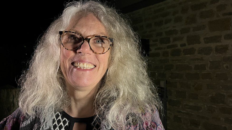 A smiling woman with glasses and curly grey hair