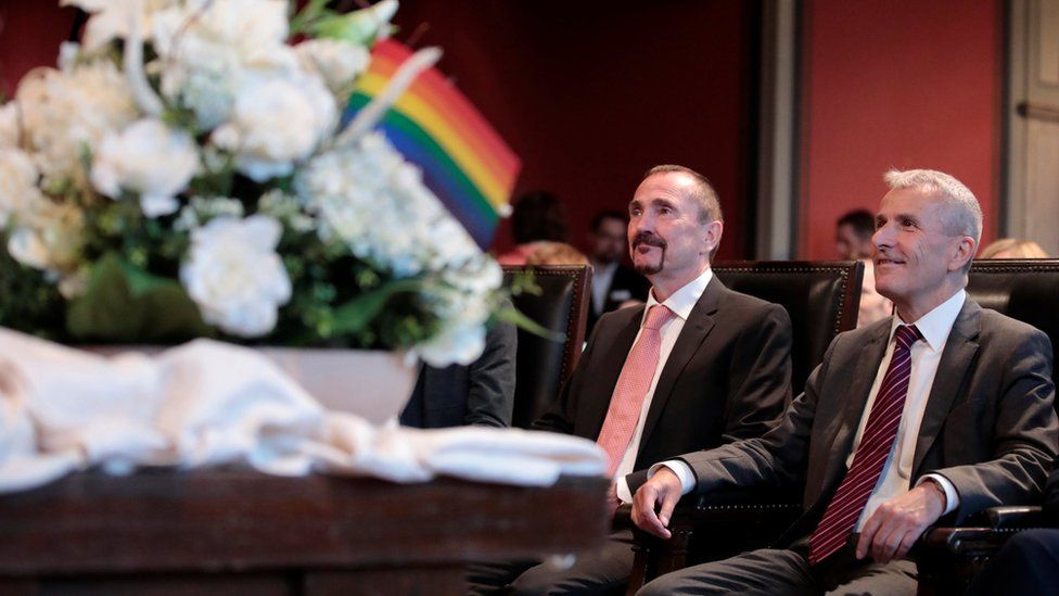 Karl Kreil and Bodo Mende sit in front of a table with flowers and rainbow flags