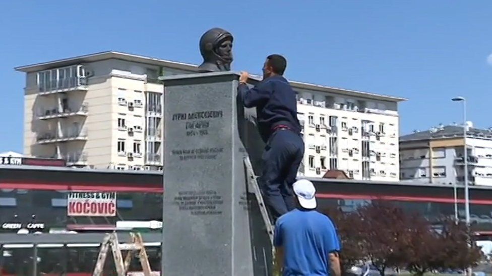 A workman climbs a ladder to remove the bust of Yuri Gagarin from its plinth