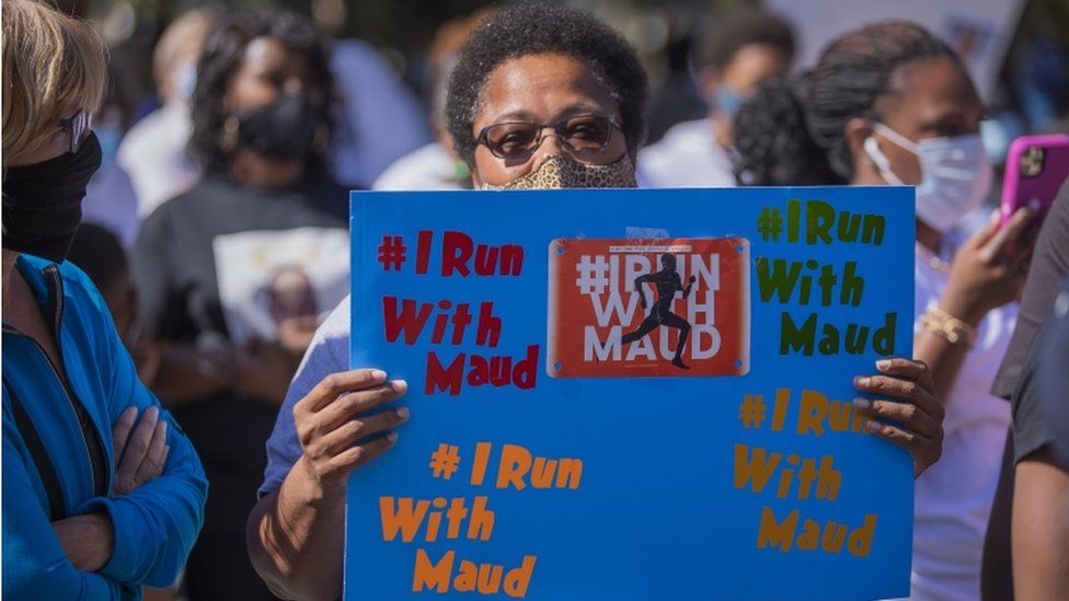 A woman holds an 'I stand with Maud sign at a protest after the shooting death of Ahmaud Arbery