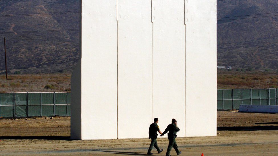 US border patrol officers walk near a prototype for the border wall with Mexico, October 2017