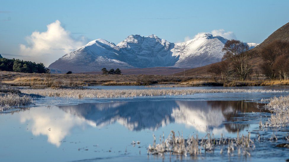 The snow-covered peak of Beinn Eighe and the mountains of Torridon are reflected in Loch Droma near Ullapool, Wester Ross.