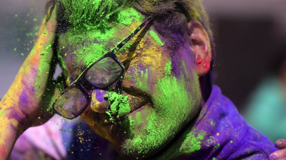 A man is covered in colours by a friend