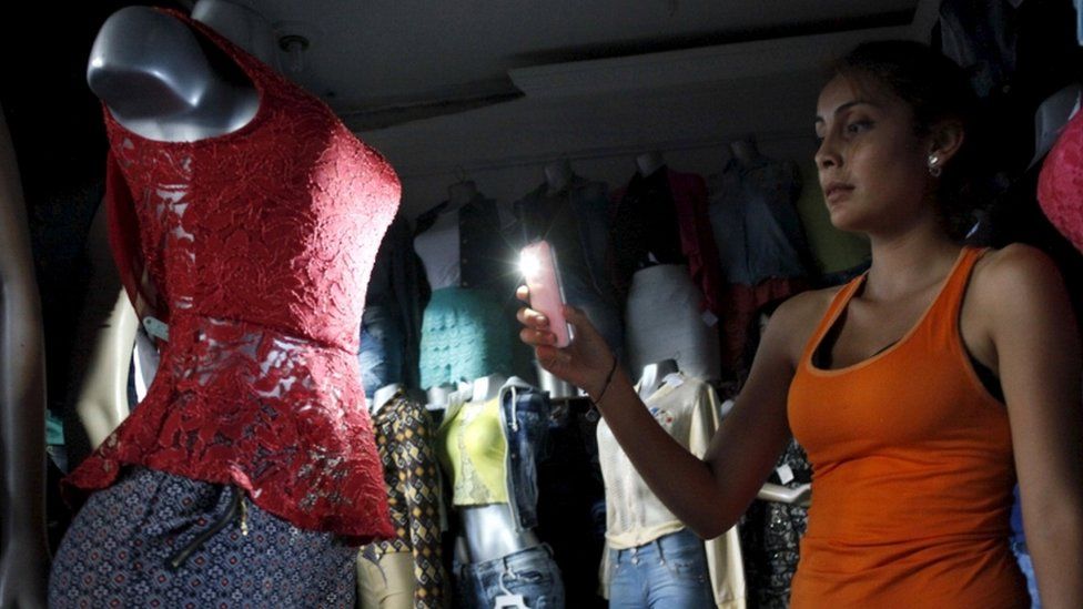 A customer uses her phone's light to look at a dress at a store during a power cut in San Cristobal, in the state of Tachira, Venezuela, April 25, 2016