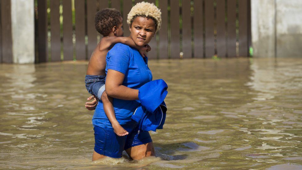 Woman carrying child wades through flooded street