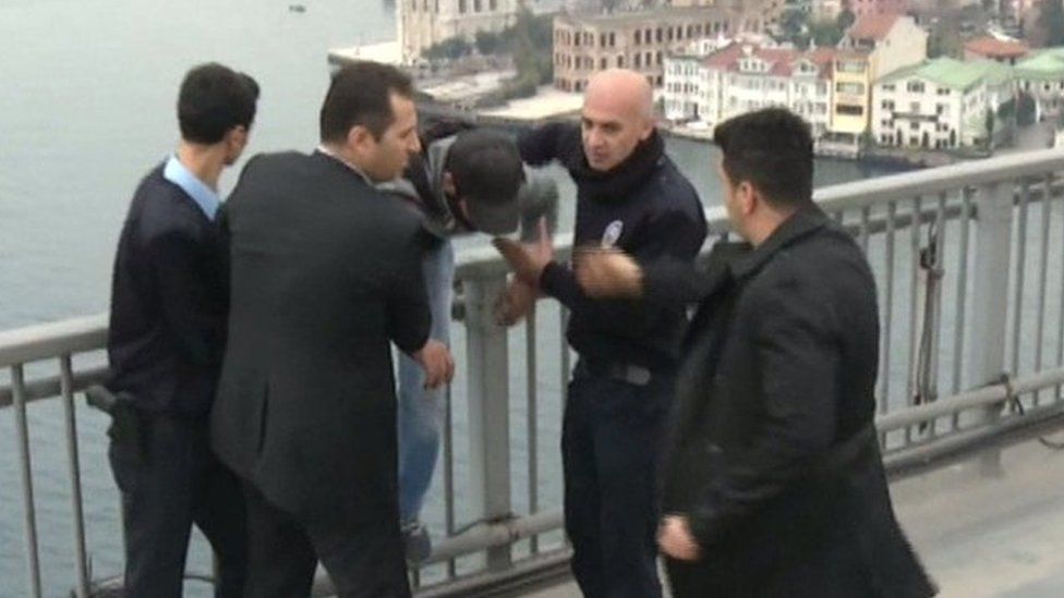 A man is escorted off the side of the Bosphorus bridge in Istanbul after President Erdogan intervened in his apparent suicide attempt on Friday