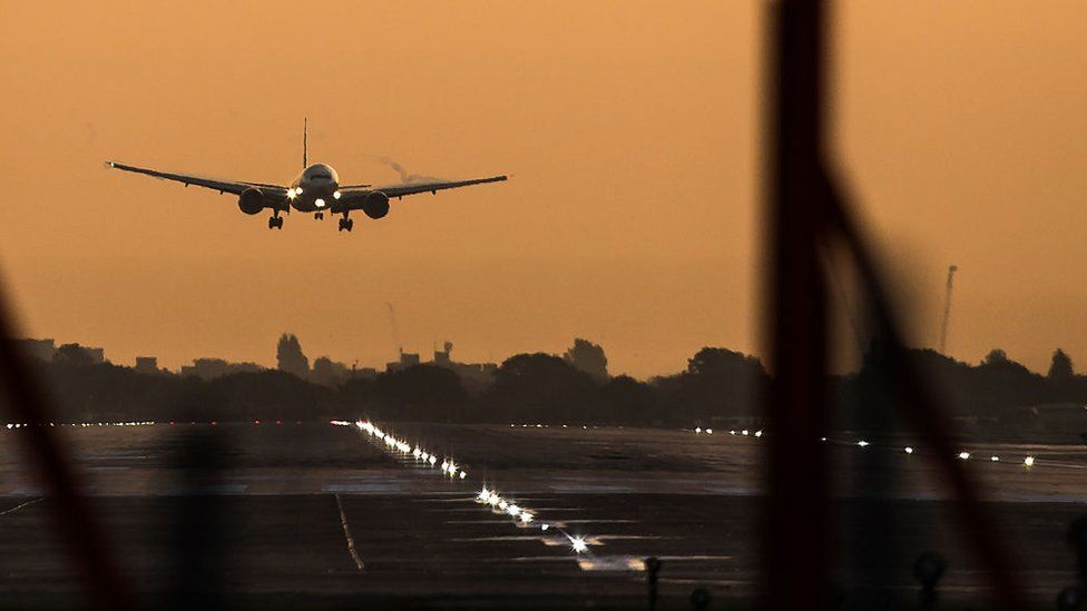 A passenger aircraft prepares to land during sunrise at London Heathrow Airport