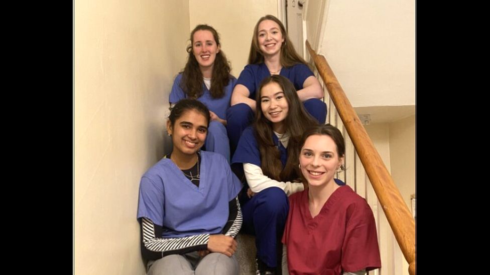 Five women dressed in scrubs sitting on the stairs