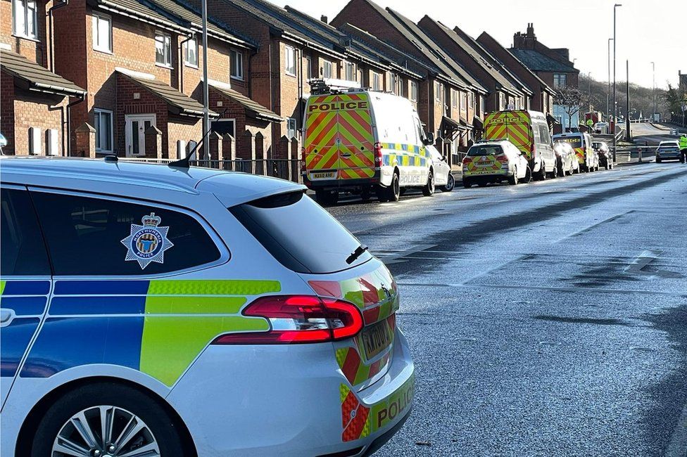 Police car in foreground with further emergency vehicles in the background, at the scene of a fatal crash