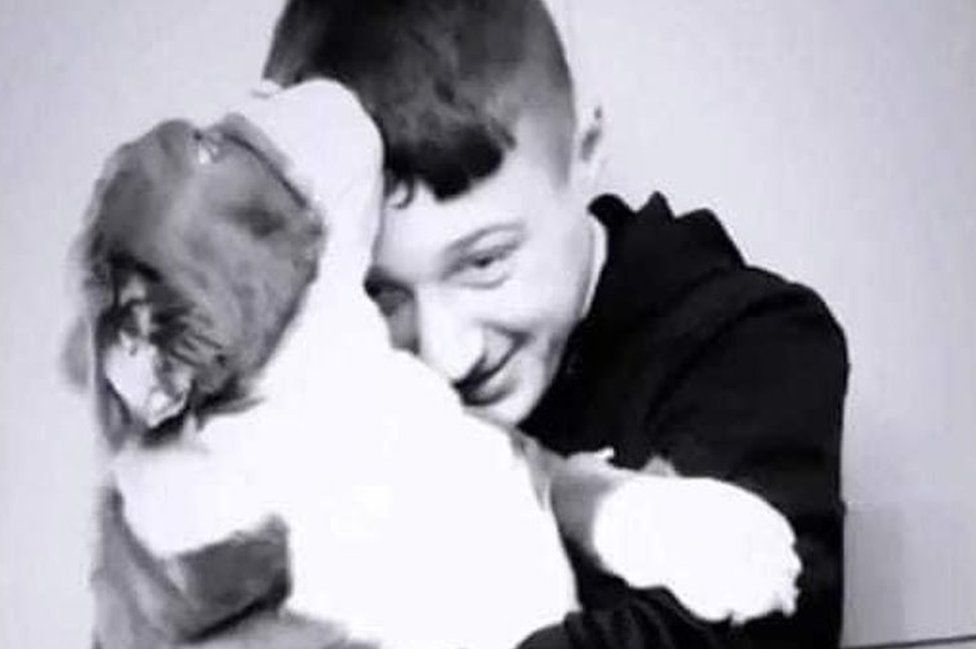 Black and white picture of a boy cuddling a dog