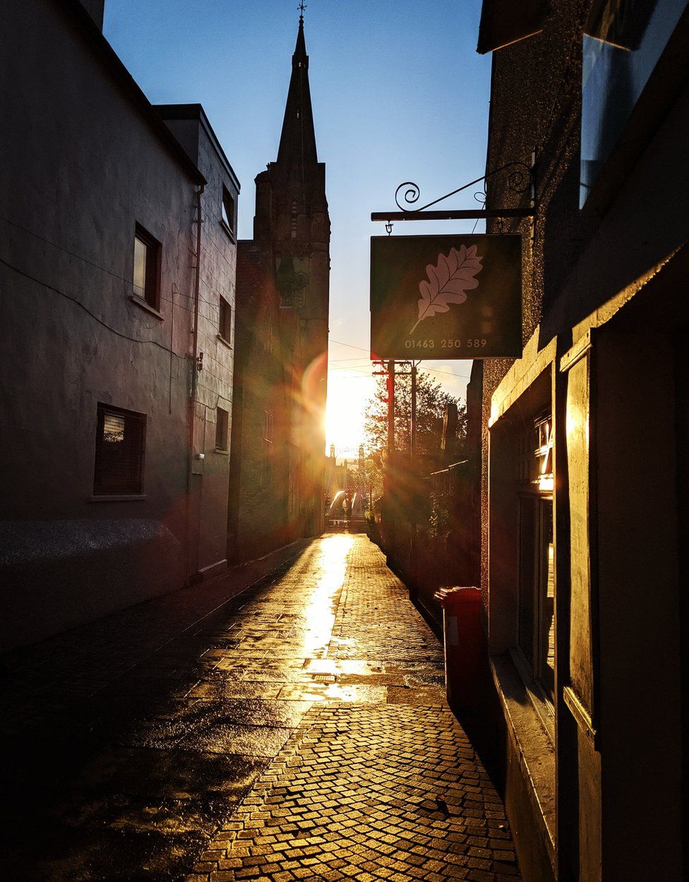 A sunset in Inverness looking down a street, with a wheelie bin in the right hand side