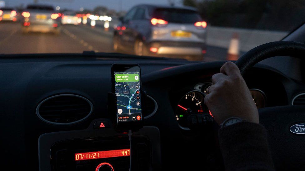Driver is using a device held in a cradle to navigate on the M4 motorway, November 2021