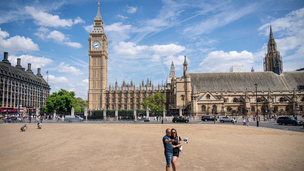 A couple pose for a selfie on the dried-up grass in Parliament Square, in Westminster, London