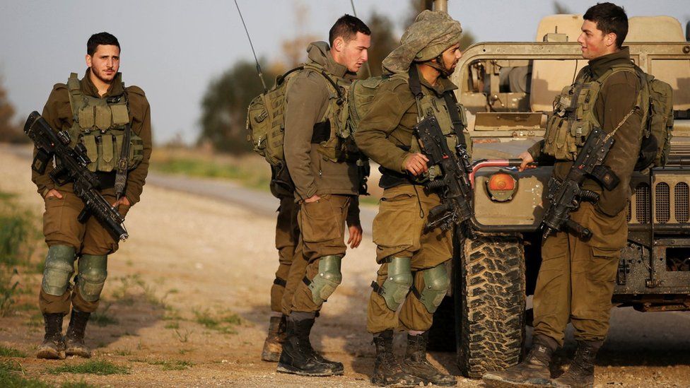 Israeli soldiers stands near a military jeep next to the border fence with the southern Gaza Strip near Kibbutz Nirim,